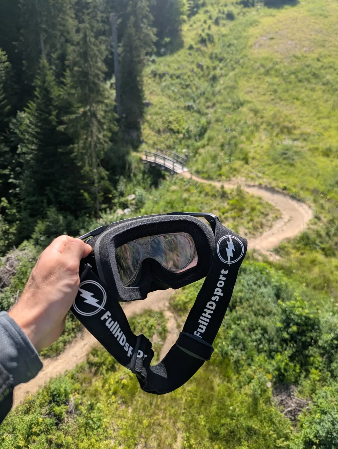 Masque à sangle FullHDsport tenu à la main au-dessus d'un sentier de forêt
